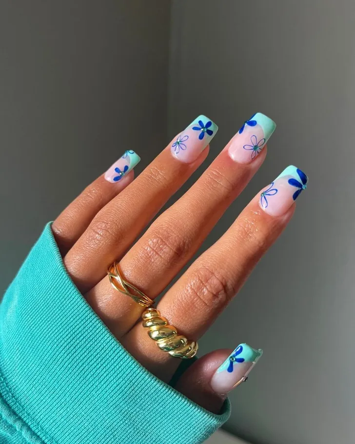 Simple floral nails with dark blue flowers and turquoise French tip - minimalist hand showcasing nude base with dark blue flower petals, featuring turquoise French tips and green leaves on almond-shaped nails